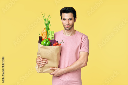 Young handsome man holding paper shopping bag full of fresh vegetables