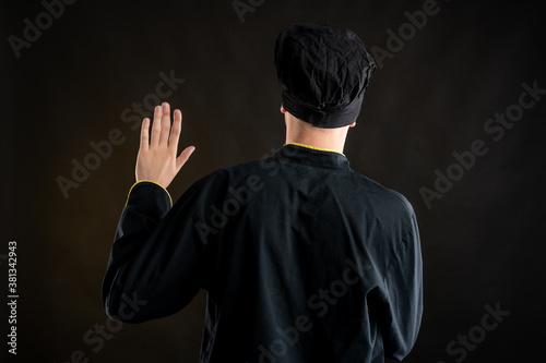 Young male dressed in a black chef suit showing oath from behind