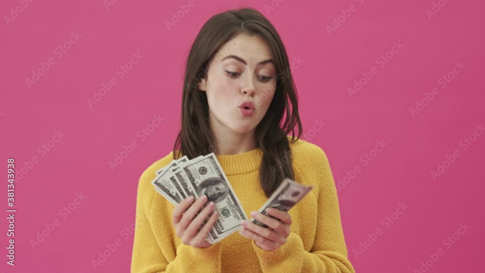 A pleased woman is counting her money standing isolated over a pink background A pleased woman is counting her money standing isolated over a pink background