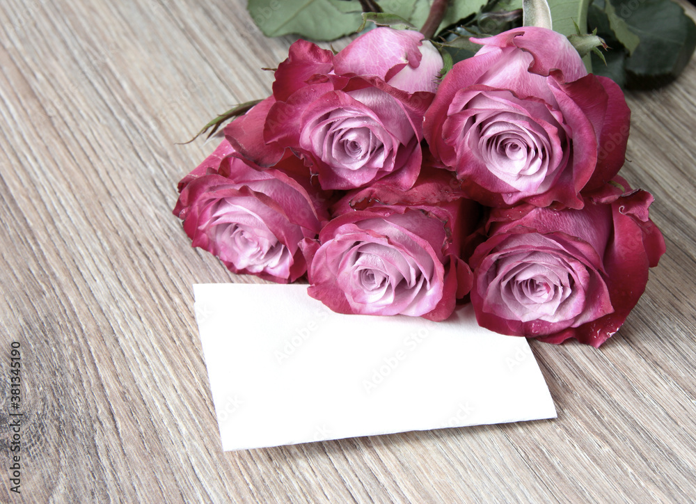 A bouquet of roses with a white leaf for writing on a wooden background.