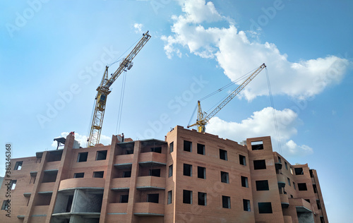 Building of a multi-storey brick house. Crane supplies construction materials to builders at a height of