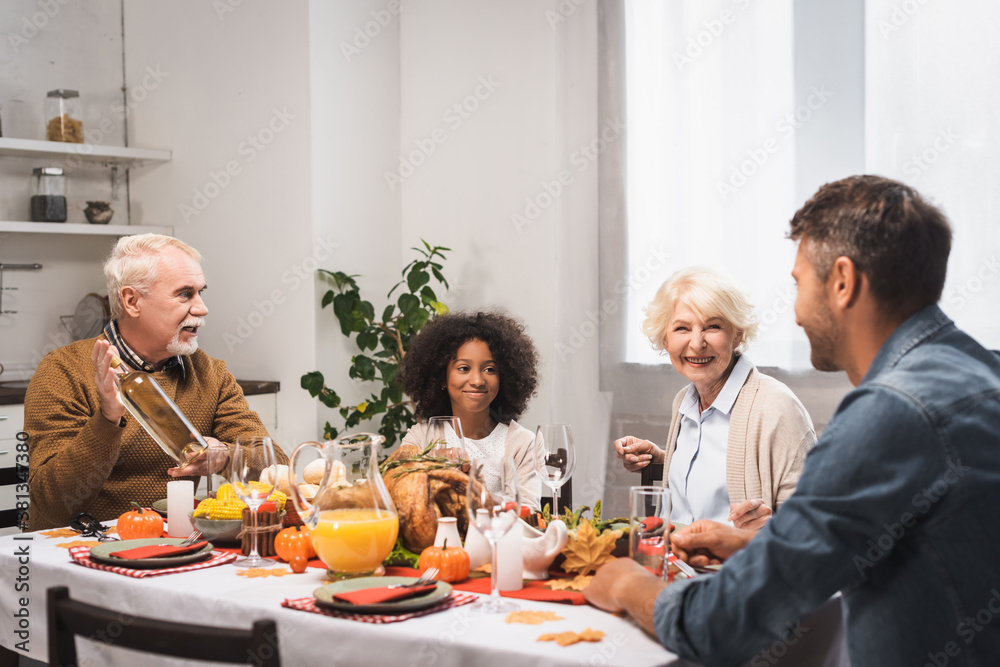 senior man holding bottle of white wine during thanksgiving dinner with multicultural family
