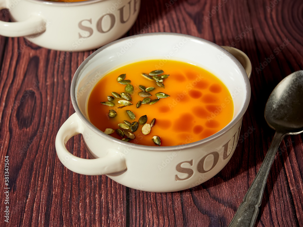 Two bowls of homemade pumpkin soup, decorated with pumpkin seeds and drops of pumpkin oil, on brown background Two bowls of homemade pumpkin soup, decorated with pumpkin seeds and drops of pumpkin oil, on brown background