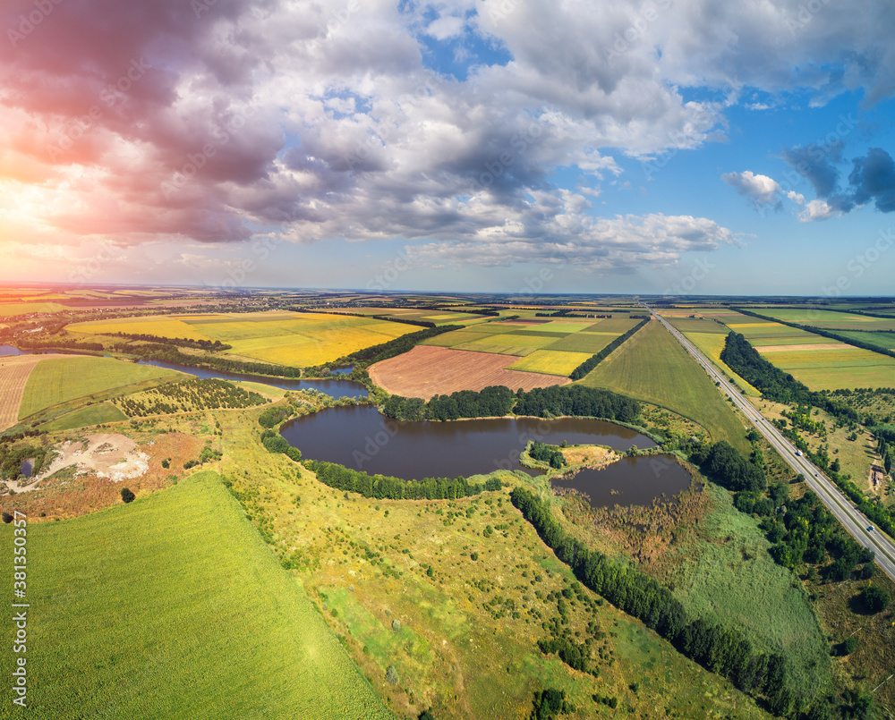Rural landscape with beautiful sky, aerial view. View of colorful arable fields, lake and highway in summer