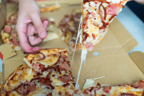 hand picking up a piece of pizza with melted cheese. order food delivery.
