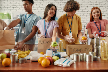 Young male and female volunteers packing food and drinks donation for homeless into paper bags, Small group of happy people working in charitable foundation