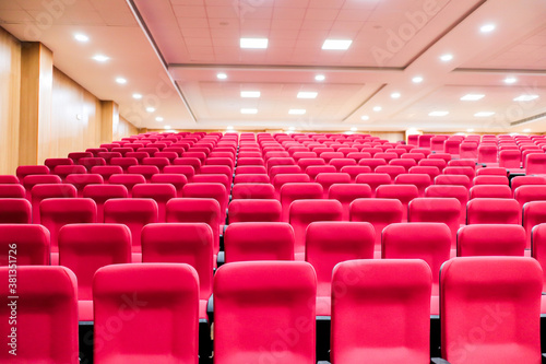 empty seats of an auditorium with red reclining rows of seats and false ceiling led lights