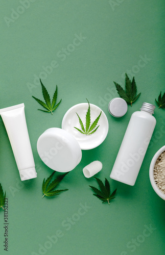 Hemp moisturizing cream in white jar with CBD oil cannabis leaf and set skin care cosmetics in white bottles tubes on green background
