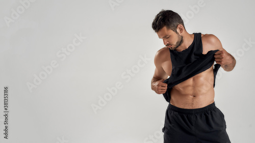 Young handsome muscular caucasian man lifting black shirt, showing his abs while posing isolated over grey background