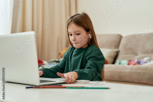 A cute girl decided to make her distance education hometask and moving a laptop on a table while sittining alone in a big bright guestroom