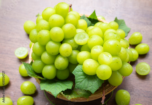 Green grape in Bamboo basket on wooden table in garden, Shine Muscat Grape with leaves in wooden background
