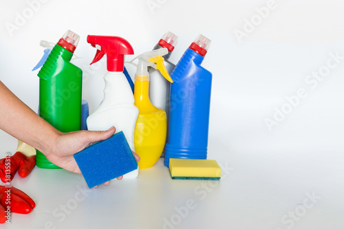 Hand with sponge and Plastic bottles with chemicals for home cleaning