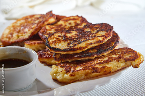 Pancakes on white plate and sweet liquid honey or caramel with a small spoon and with background. Delicious fried flour food. Unhealthy and harmful, but very tasty food.
