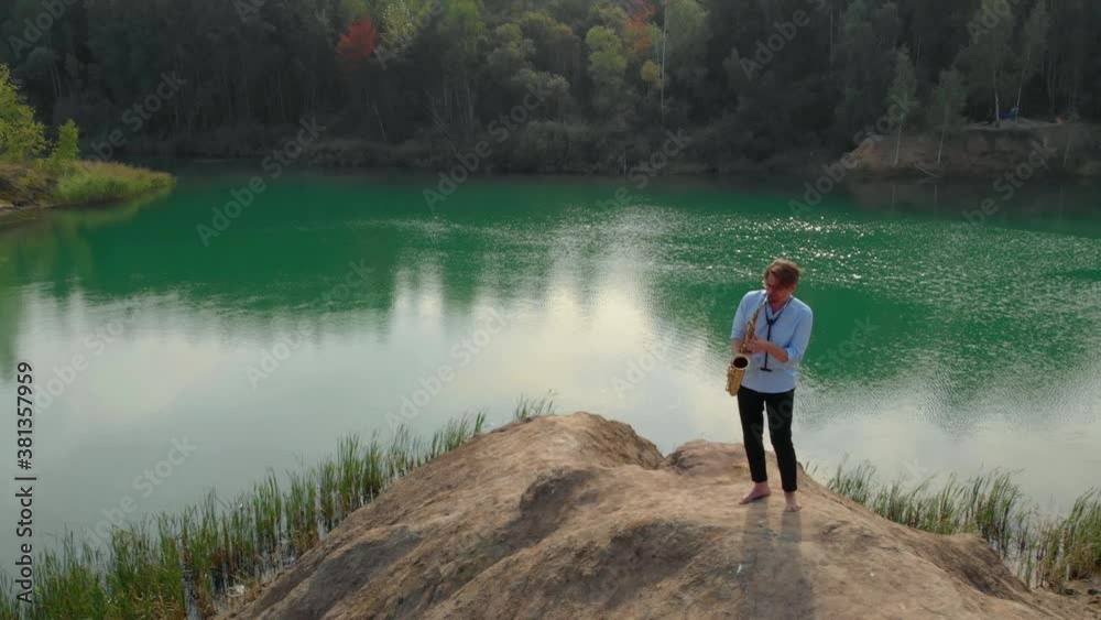 amazing landscape with forest and green lake and man with saxophone on hill, aerial shot amazing landscape with forest and green lake and man with saxophone on hill, aerial shot