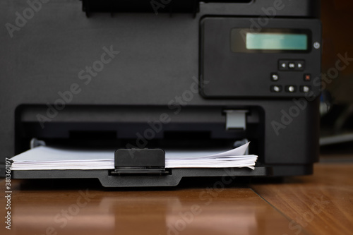 Workspace with a printer with blank sheets of paper on a wooden table, selective focus, copy space