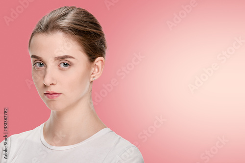 Serious beautiful girl in white t-shirt posing on pink background