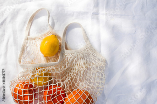 juicy citrus fruits in a string bag in the sun on a white tablecloth. Healthy diet. Vitamins. Copy space.