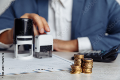 Businessman approves a profit contract. Stack of coins, contract and stamps on desk. Economy and management financial concept