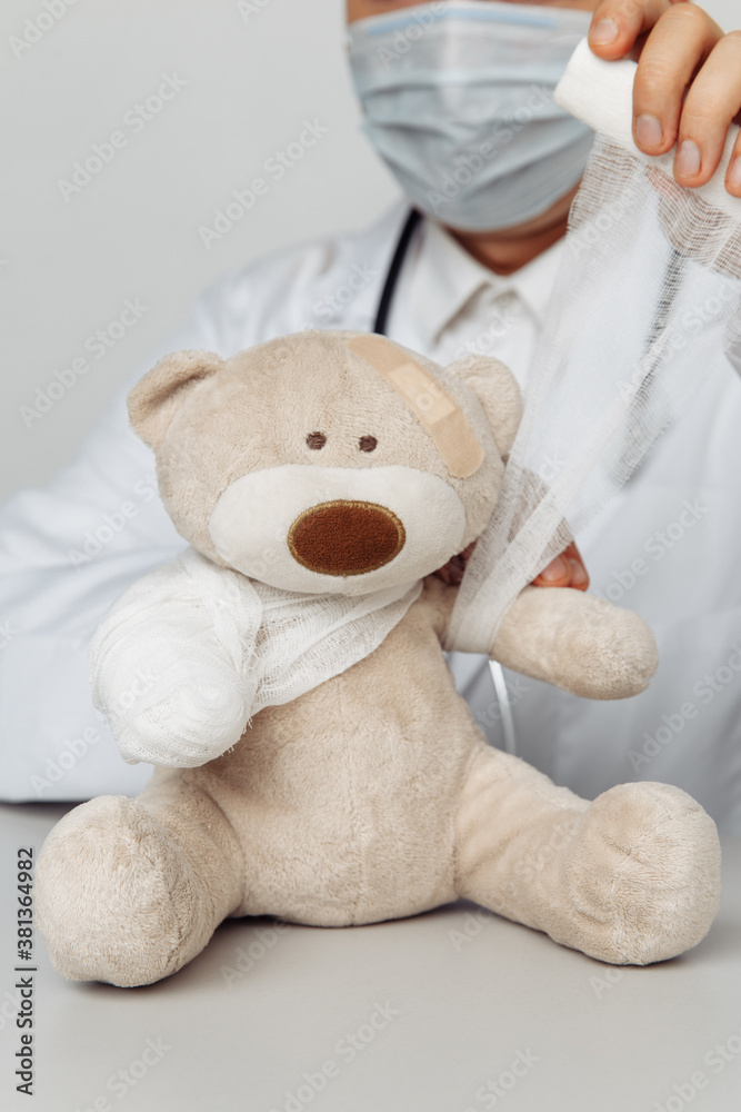 Pediatrician in mask bandage teddy bear in medical office. Close-up. Children healthcare concept