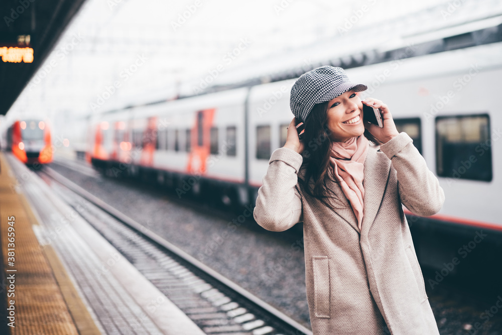 Young woman in winter coat and hats with phone in hand waiting on railway station for train. A girl is wating a train in a trian station at Europe.