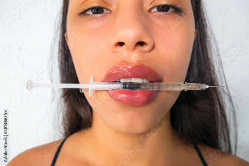 Close-up of a beautiful young woman's face with a syringe in her mouth. Injection of hyaluronic acid collagen to correct, pamper and enhance the lips