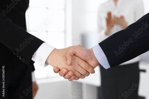 Businessman and woman shaking hands with colleagues at the background. Handshake at meeting in office. Concept of success in business