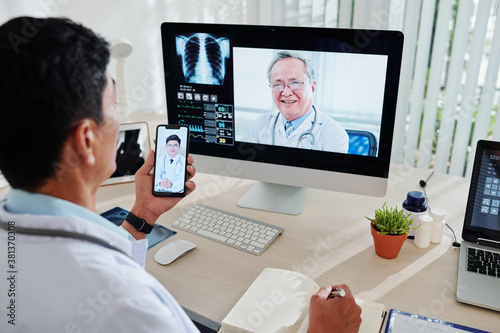 Mature Vietnamese doctor video calling his two colleagues to discussing difficult case of bilaterial pneumonia photo