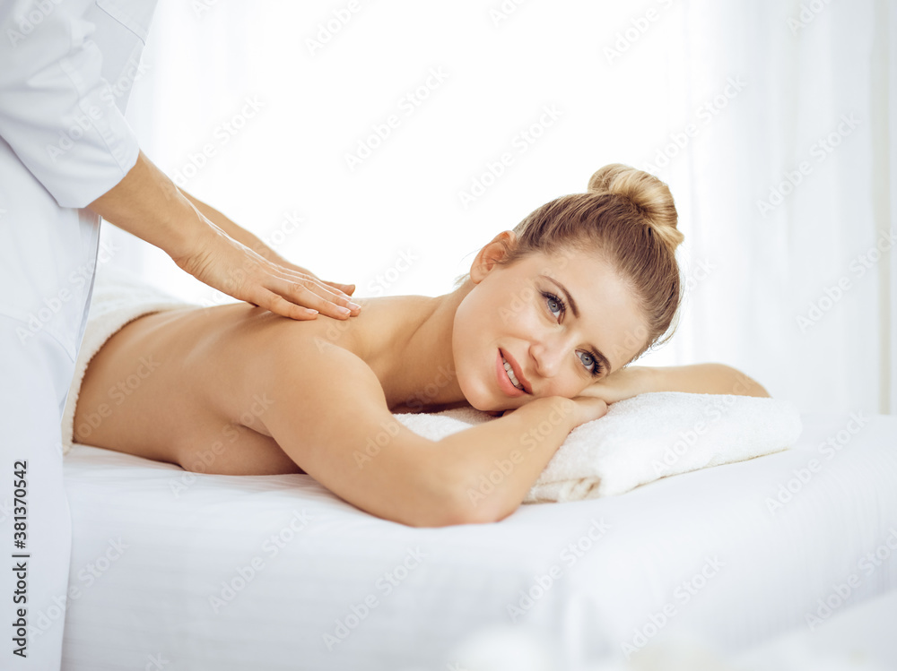 Young and blonde woman enjoying massage of back in spa salon. Beauty concept Young and blonde woman enjoying massage of back in spa salon. Beauty concept