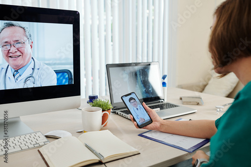 Female cardiologist using laptop and smartphone when video calling her colleagues to discuss diffucult case photo