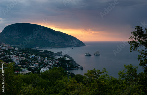 Sea bay with rocks "Adalary" sticking out of the sea. Town on the shore. Morning, calm sea, from behind Mount Ayu-Dag (Bear Mountain) the rays of the rising sun. Gurzuf, Yalta, Crimea. © Aleksandr
