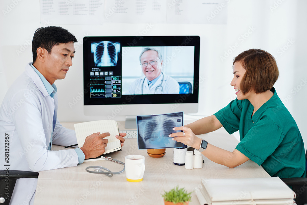 Radiologist showing lungs x-ray to colleague at online meeting with experienced oncologist