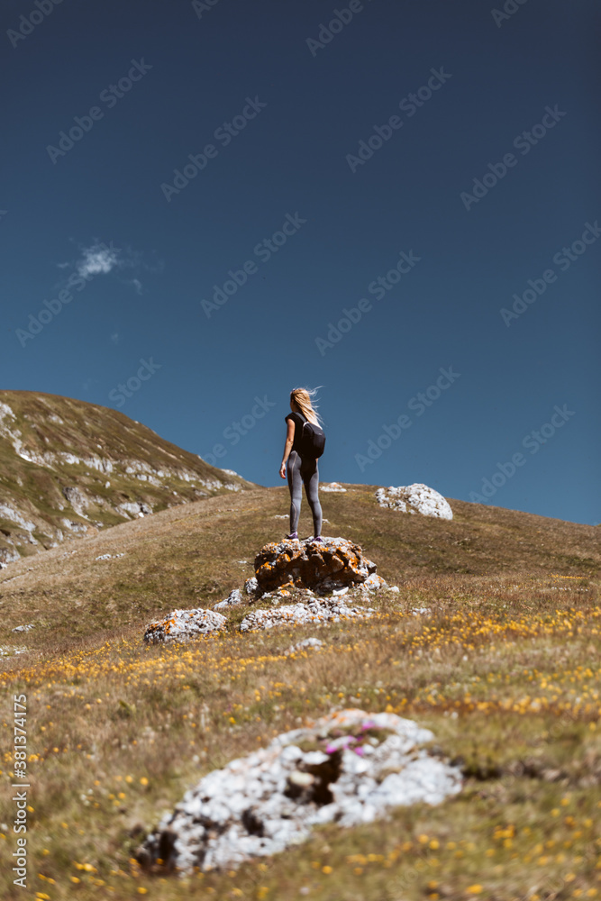 Fit young woman hiking in the mountains standing on a rocky summit ridge with backpack and  looking out over an alpine landscape. Vintage,healthy lifestyle concept.