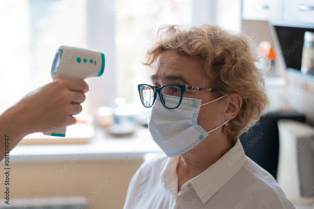 The doctor measures the temperature of an elderly woman with an electronic thermometer