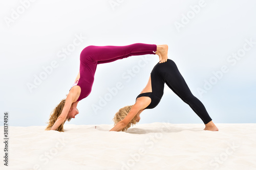 Two beautiful young women performing steamy yoga standing on the sand