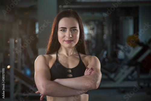 Confident strong beautiful young muscular woman crosses arms on her chest in the gym ready for a workout. look at the camera. Concept of girl power, women's sports, workout, women's fitness trainer