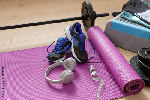 Fitness tools dumbbells yoga mat and shoes on a wooden floor in natural light. Healthy living concept.