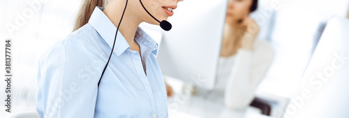 Female call operator is using computer and headset for consulting clients online, close-up. Group of diverse people working as customer service occupation photo