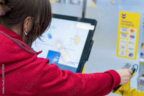 Girl in a medical mask from the virus, pays with a credit card in the store terminal. Contactless purchase of goods. photo