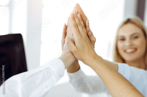 Group of business people joining hands or giving five to each other after meeting or negotiation in sunny office