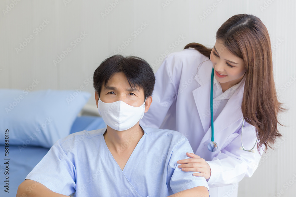 Asian doctor woman talking with a man patient who wear face mask about his health symptom while he sit on wheelchair at hospital.