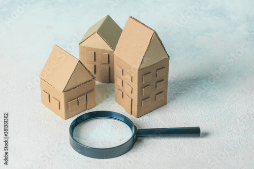 Finding or choosing the best home. Magnifying glass and cardboard miniature houses. Sale or rental of housing.