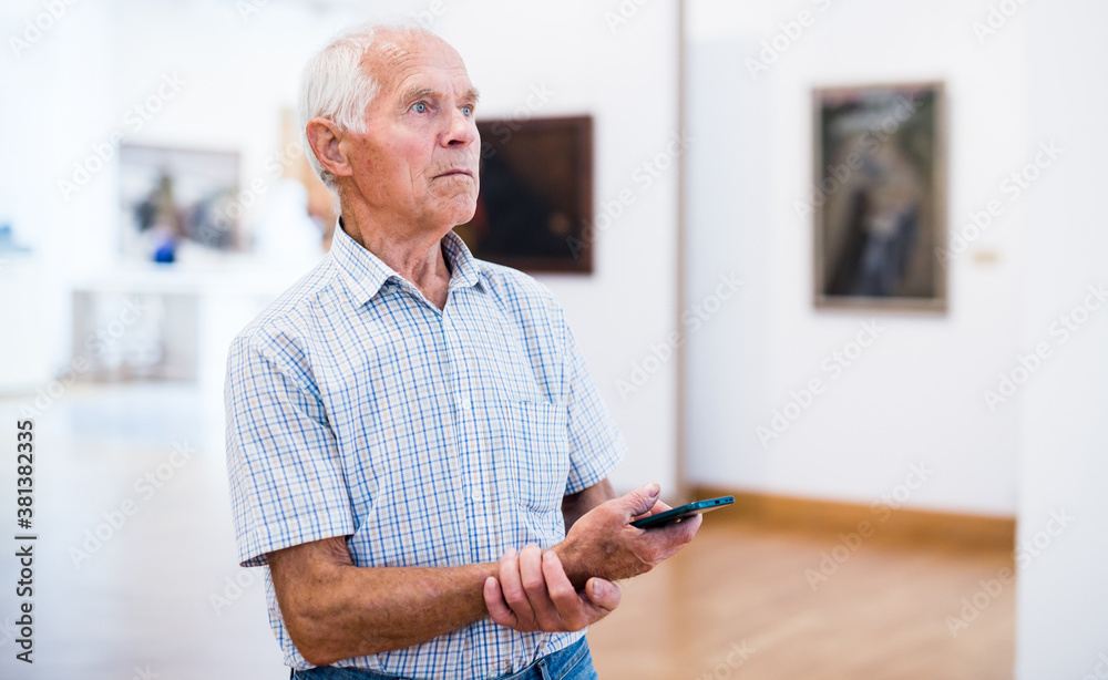 mature European man examines paintings in an exhibition in hall of an art museum mature European man examines paintings in an exhibition in hall of an art museum