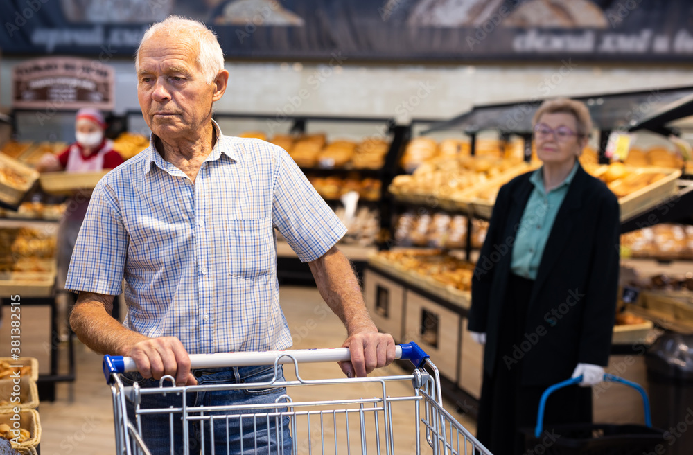 older man shopping buns and bread in bakery section of supermarket