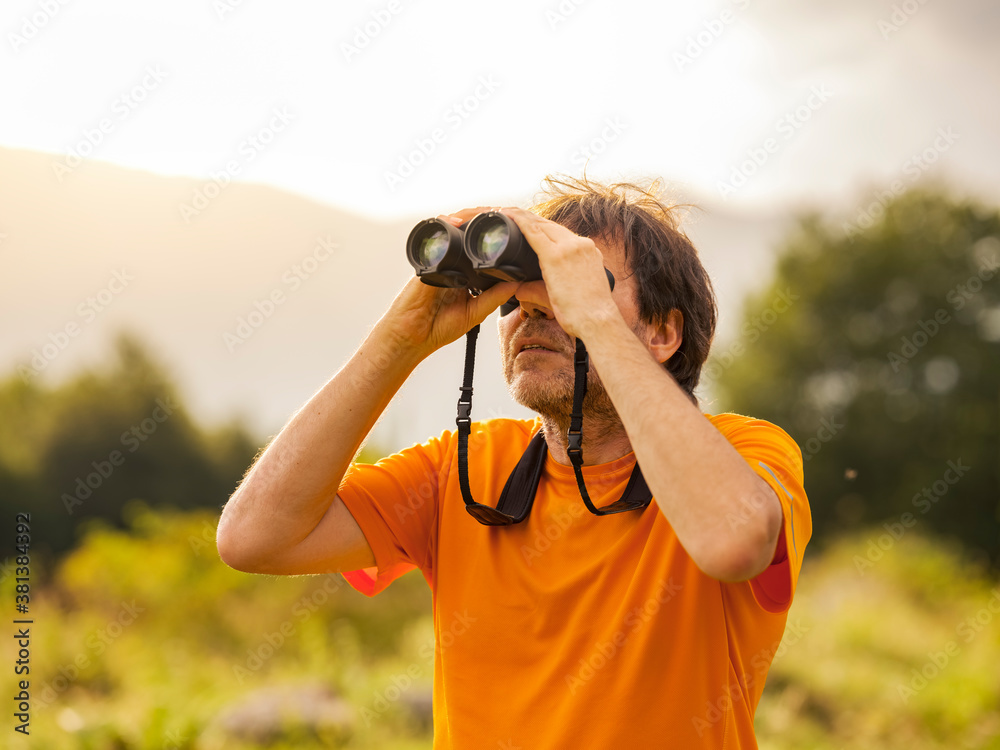 The hiker does bird watching with binoculars in the mountain nature park in search of birds of prey. Man scans the sky with binoculars. Concept of person looking to the future. The hiker does bird watching with binoculars in the mountain nature park in search of birds of prey. Man scans the sky with binoculars. Concept of person looking to the future.