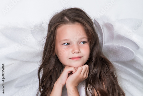  A cute dark-haired girl in a white dress with white wings. Dreaming. Close-up.
