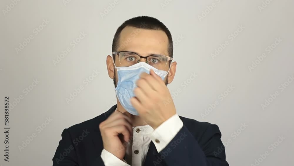 A young successful businessman puts on a medical protective mask while talking with partners. A young successful businessman puts on a medical protective mask while talking with partners.