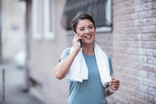 Young female athlete jogging outdoors. Beautiful woman talking to the phone.