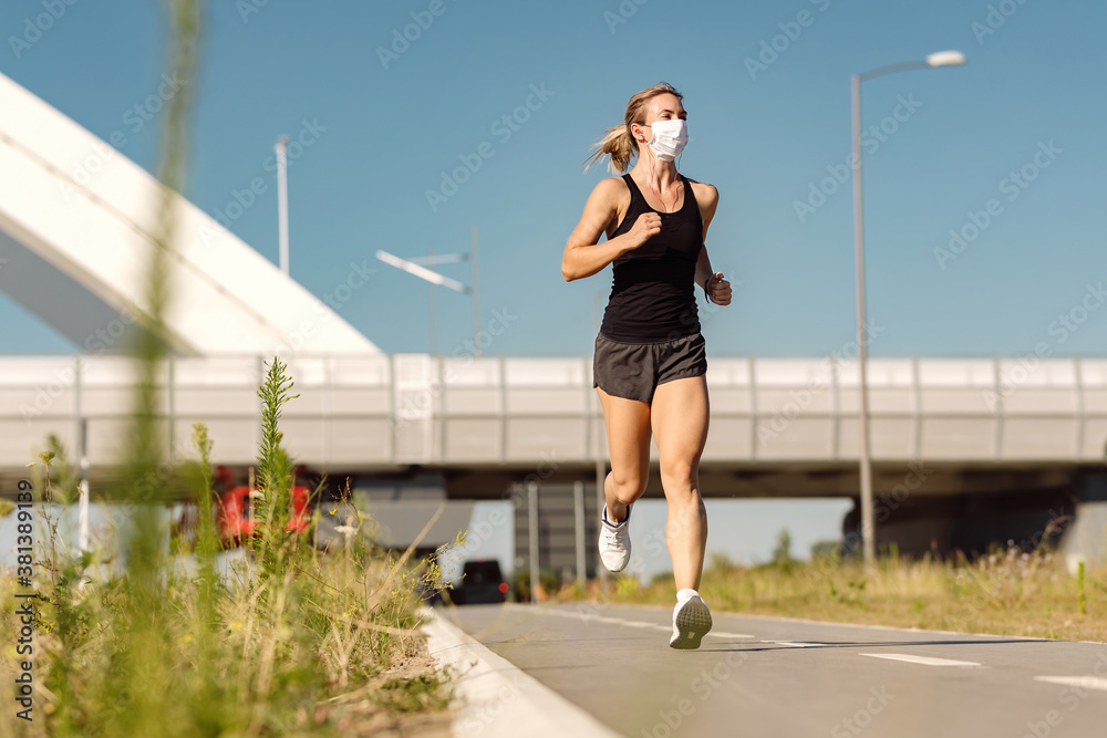 Athletic woman with protective face mask running outdoors.