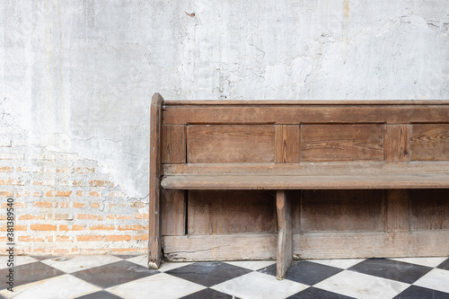 close up view of old wooden bench on checkered pattern marble tiles floor with brick and cement wall background in church