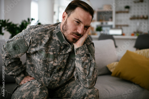 Depressed soldier sitting on sofa in living room. Young marine having PTSD..